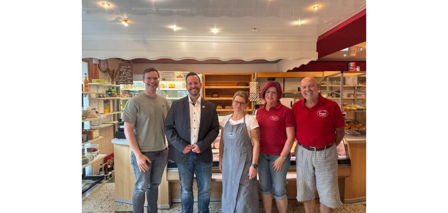 Betriebsbesuch in der Bäckerei Engels in Nachtsheim (v.l.n.r.): Alexander Röser (Wirtschaftsförderer) und Bürgermeister Timo Kanzinger mit Sarah Hilger-Felderhoff sowie den Inhabern Helga und Werner Engels Plakat mit Verminhinweis für das nächste Treffen der Wacholderwacht Osteifel am 25.09.2026