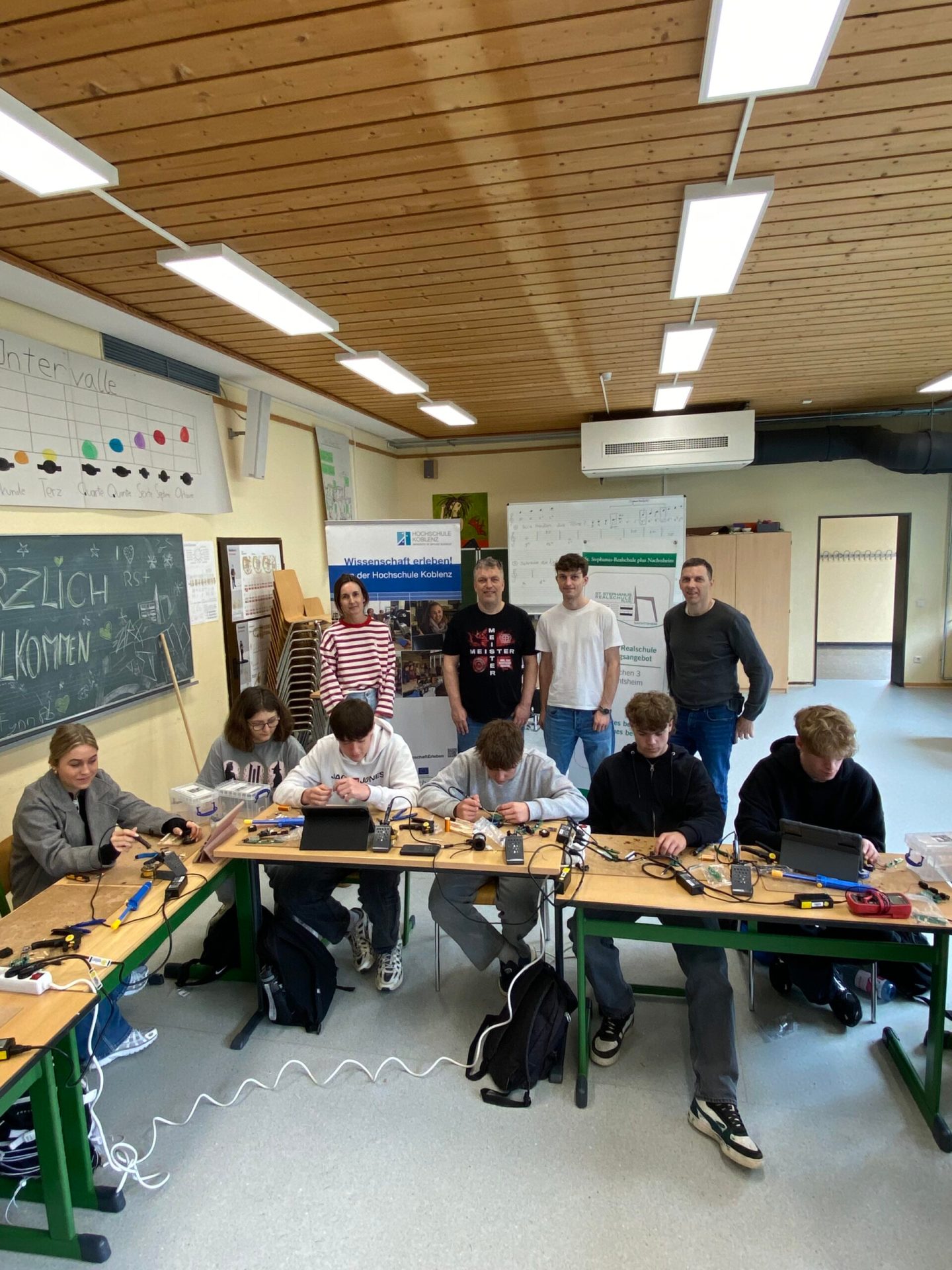 Schülerinnen und Schüler der Klasse 9a der Realschule plus Sankt Martin in Nachtsheim experimentieren mit technischen Alltagsgegenstände wie einer Smartphone-Boombox, einem Lauflicht oder einer Hochspannungs-Tesla-Spule, unterstützt von Schulleiter Michael Walo sowie dem Projektleiter des MINT-Mobils, Prof. Dr. Johannes Stolz, und einem Studierenden der Elektrotechnik von der Hochschule Koblenz.