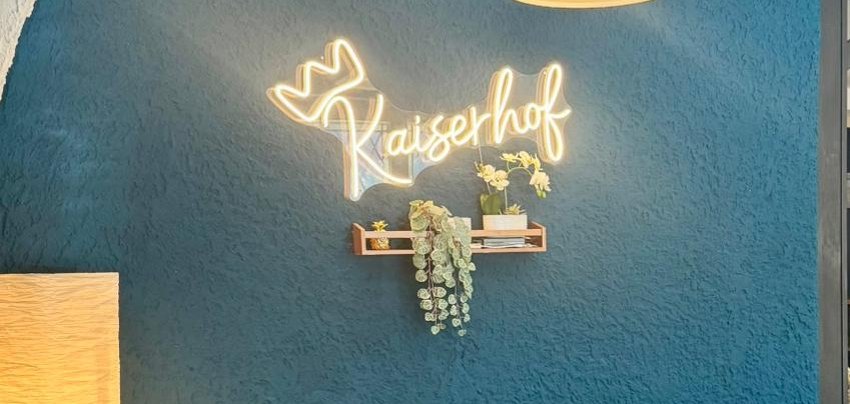 Beleuchtetes Logo vom Kaiserhof an der blau gestrichenen Wand